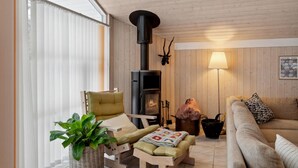 Un salon chaleureux avec un poêle à bois, un fauteuil vert, un canapé et une table agrémentée d’une plante.