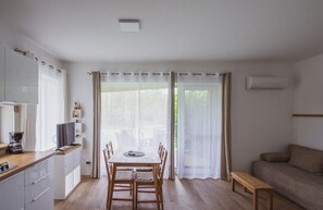 A modern, well-lit room with a wooden dining table and chairs, a sofa, and a kitchenette area.