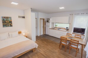 Une chambre d’hôtel moderne comprenant un lit, une table à manger avec des chaises, un coin cuisine avec un four à micro-ondes et un réfrigérateur, ainsi qu’un tableau accroché au mur.