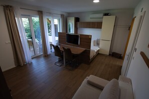 A modern hotel room with a wooden floor, a bed, a desk with a TV, a sofa, and a balcony with a view of greenery. - Comfort Studio with Patio (Visoko)