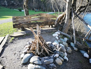 Un área de estar rústica al aire libre con un banco de madera y un hogar rodeado de rocas.