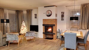 A cozy living room with a fireplace, a Christmas tree, and a dining area with chairs and a table. - Panoramic apartment with Terrace (Visoko)