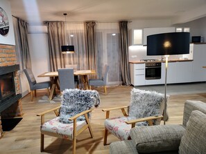 Moderni olohuone, jossa on takka, ruokailutila ja keittiö sekä litteänäyttöinen televisio.