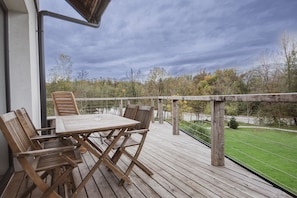 A wooden deck with a table and chairs, overlooking a grassy area and trees.