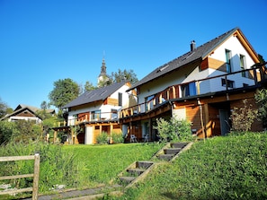 Une maison à deux étages avec un balcon, une terrasse en bois et une cour gazonnée.
