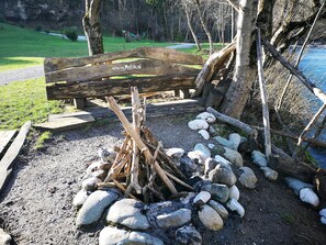 Un espace extérieur rustique aménagé avec un banc en bois et un foyer entouré de pierres.