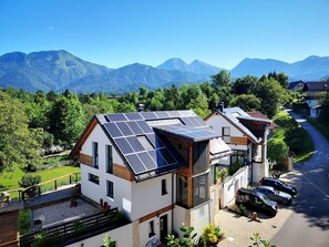 Ein modernes Haus mit Solaranlage auf dem Dach, umgeben von üppiger Vegetation und Bergen im Hintergrund.