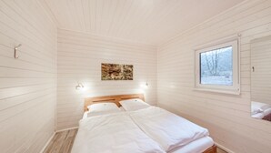 A bedroom with a wooden bed, a window with a view of trees, and a painting on the wall.