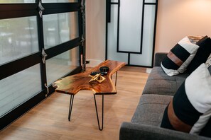A modern living room with a wooden coffee table, a grey sofa, and a large window with metal frames.