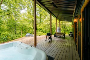 A wooden deck with a hot tub, outdoor seating, and a view of a forest.