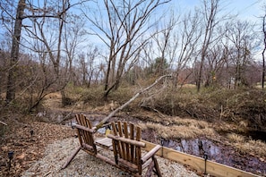 A wooden chair and a wooden bench near a stream in a forested area. - The Juice Box | Hocking Hills, Container Cabin (Creola)