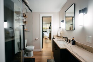 A modern bathroom with a glass shower enclosure, a white toilet, a wooden floor, and a marble countertop with a sink and mirror.