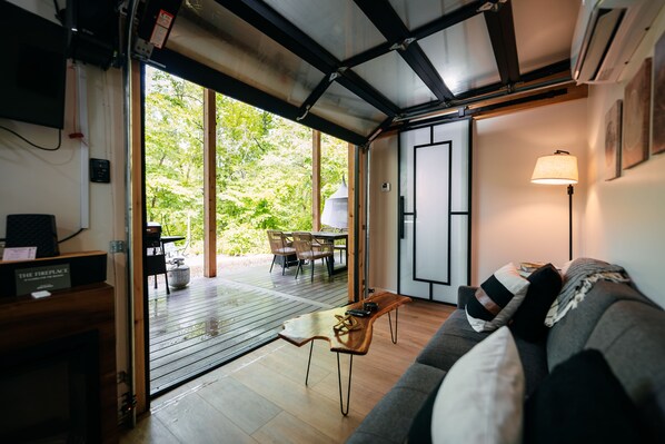 An open-plan living area with a sofa, a coffee table, and a dining table with chairs. There is a sliding door leading to an outdoor deck.