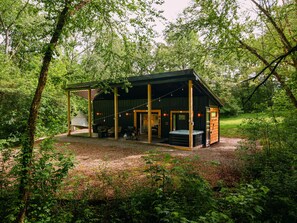 A rustic cabin with a covered patio, outdoor seating, and a hot tub. - The Juice Box | Hocking Hills, Container Cabin (Creola)