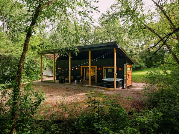 A rustic cabin with a covered patio, outdoor seating, and a hot tub.