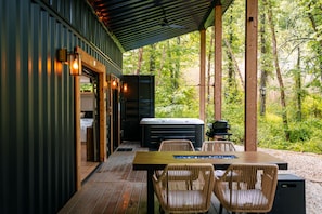 A covered outdoor area with a hot tub, wicker chairs, and a wooden table.