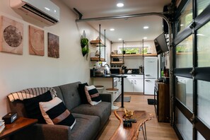 A compact living space with a sofa, coffee table, kitchen area, and a large window.