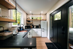 Una cocina compacta con armarios blancos, una encimera negra y un refrigerador negro.