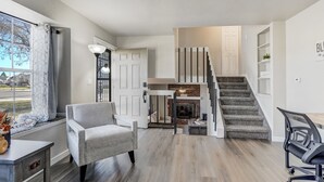 A modern living room with a grey armchair, a dining table, and a staircase leading to a loft area with a fireplace. - Pueblo Place (Pueblo)