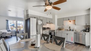 A modern kitchen with stainless steel appliances, a dining area with a round table, and a ceiling fan. - Pueblo Place (Pueblo)