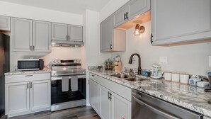 A modern kitchen with stainless steel appliances, marble countertops, and light grey cabinetry. - Pueblo Place (Pueblo)