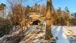 A cabin with a wooden deck and a large window, surrounded by trees and snow. - 3 bedroom gorgeous home in Ullared (Ullared)
