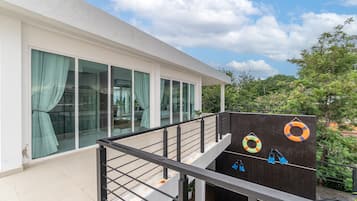 A modern building with large windows, a balcony with a metal railing, and a view of trees and a clear sky.