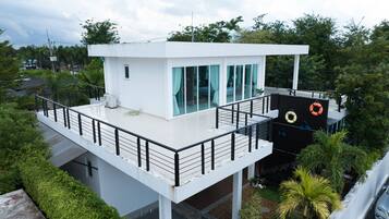 A modern two-story building with a flat roof, large windows, and a balcony with a railing.