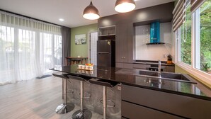 Une cuisine moderne dotée d’un îlot central, d’appareils électroménagers en acier inoxydable et offrant une vue sur la verdure environnante.