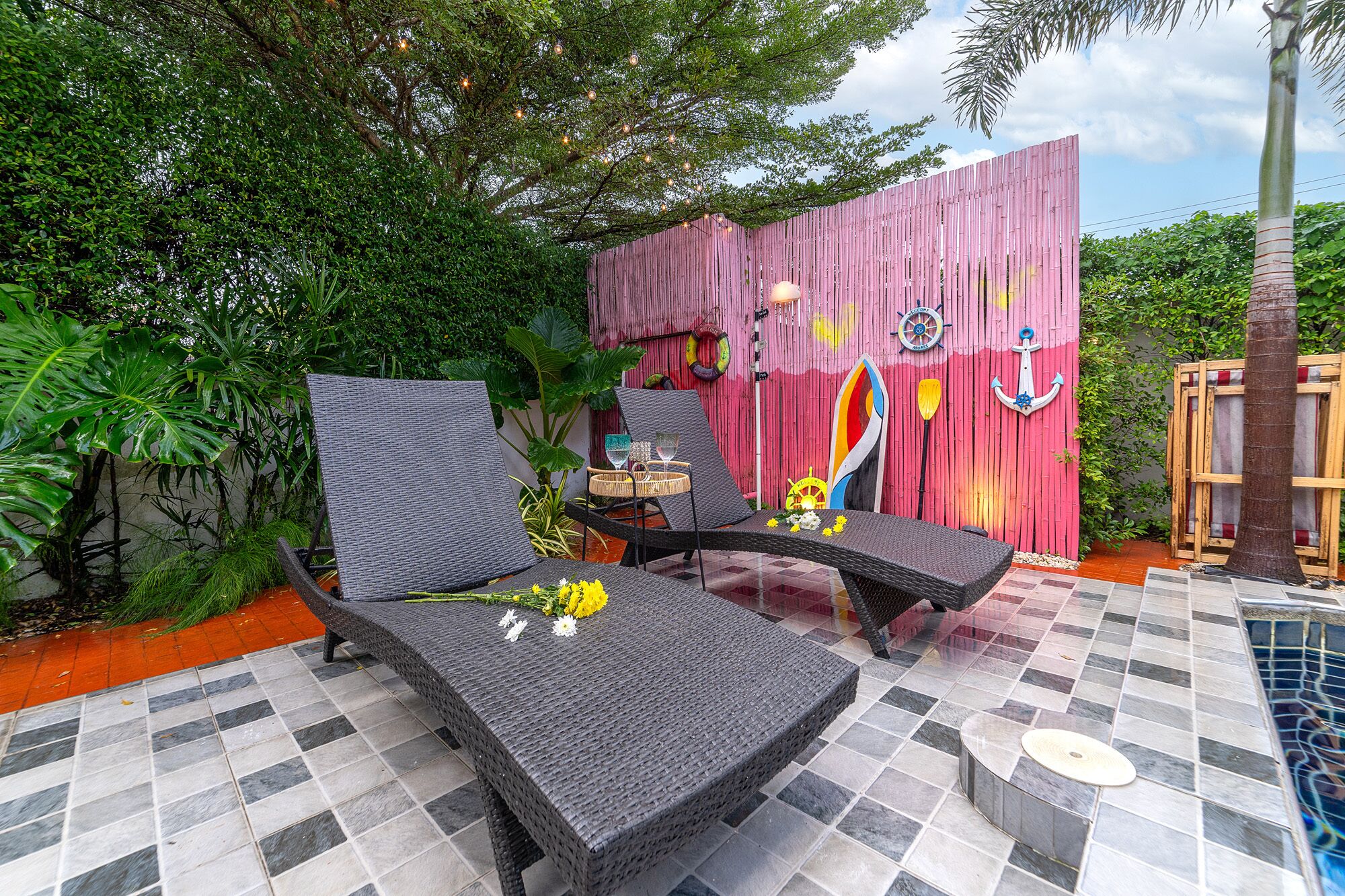 Eine Terrassenfläche mit zwei Liegestühlen, einem kleinen Tisch und einer Wand mit maritimen Dekorationselementen.