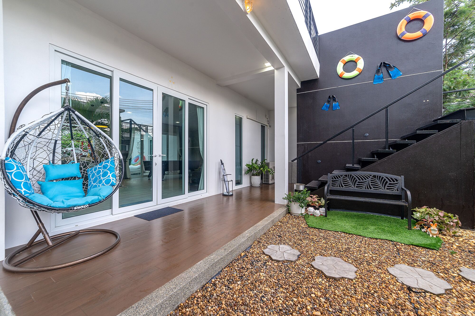 A modern house with a hanging chair, a staircase, and a garden area with pebbles and stepping stones.