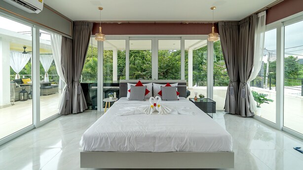Une chambre moderne dotée d’un grand lit, d’un balcon avec coin salon extérieur et de grandes fenêtres.
