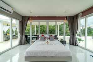Ein modernes Schlafzimmer mit einem großen Bett, einem Balkon mit Sitzgelegenheit und großen Fenstern.