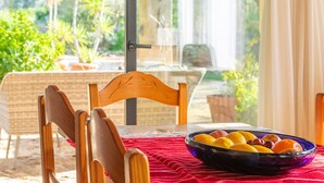 Een eettafel met een fruitschaal, een houten stoel en uitzicht op groen.