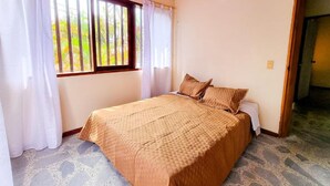 A bedroom with a bed, curtains, and a view of greenery outside. - Hostal - Casa Rionegro (Rionegro)