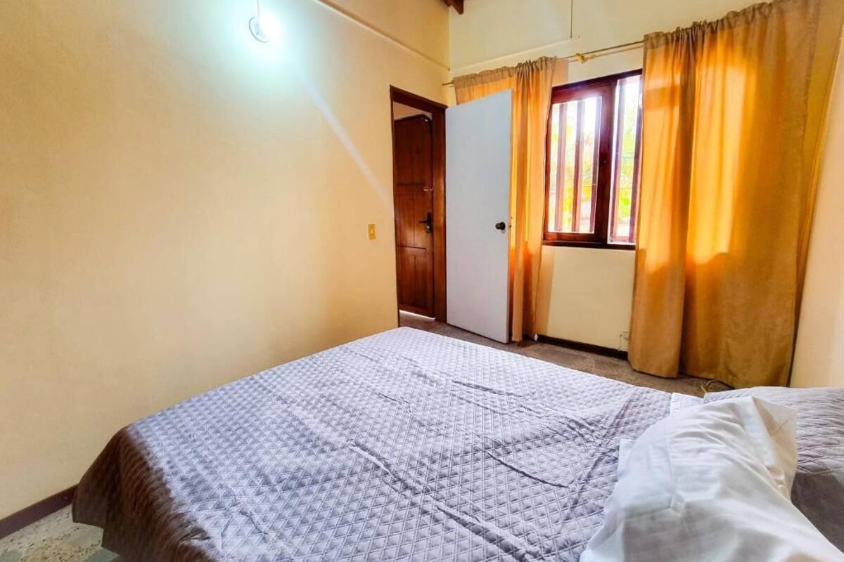 A bedroom with a bed, a window with curtains, a door, and a ceiling light.