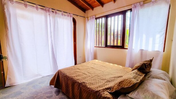 A bedroom with a bed, curtains, a window, and a wooden ceiling. - Hostal - Casa Rionegro (Rionegro)