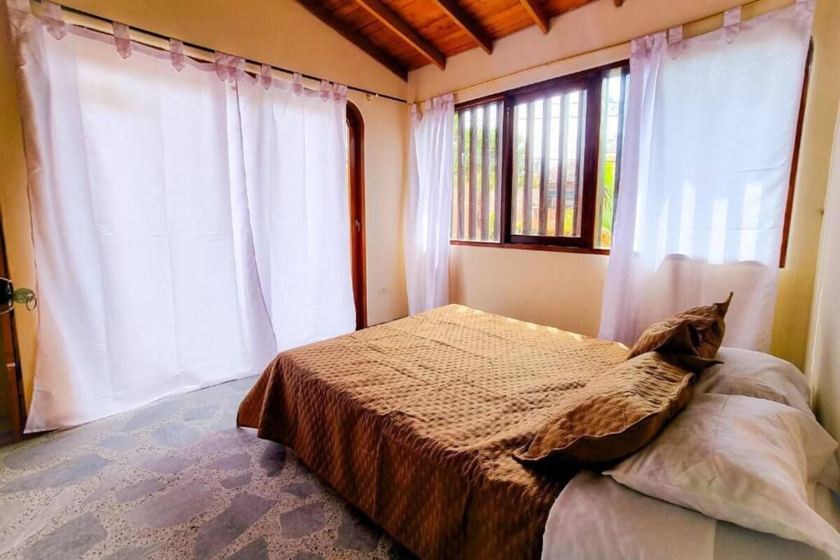 A bedroom with a bed, curtains, a window, and a wooden ceiling.