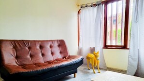A room with a brown leather sofa, a small wooden table, and a window with curtains. - Hostal - Casa Rionegro (Rionegro)