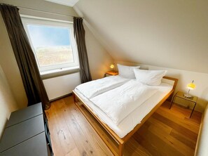 A bedroom with a bed, a nightstand, a lamp, a window with curtains, and a radiator.