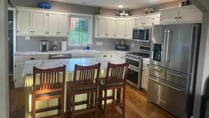 A modern kitchen with white cabinets, a central island with bar stools, stainless steel appliances, and a large window providing natural light. - Charming Farmhouse In Quarryville,PA

 (Quarryville)