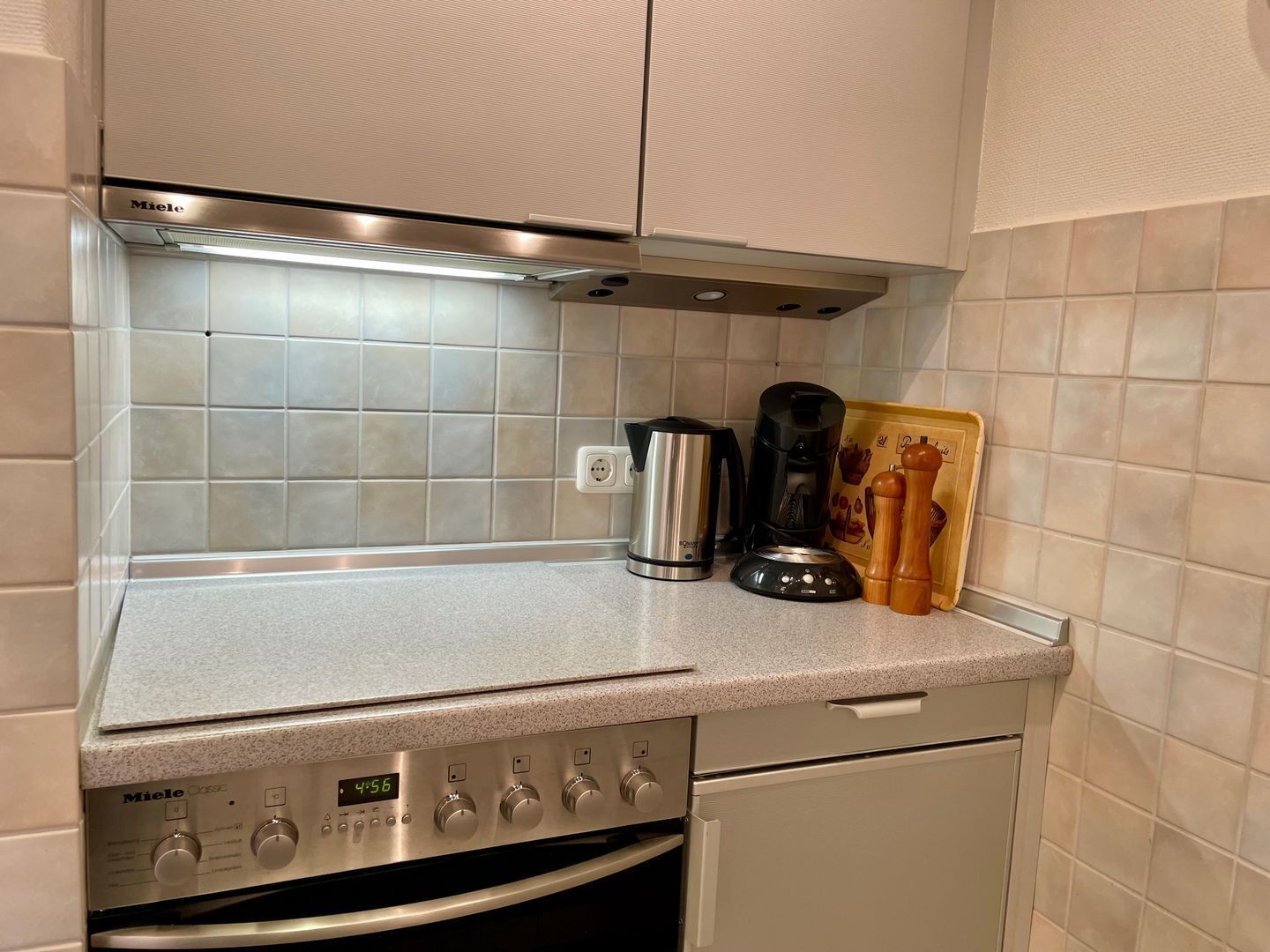 Ett litet kök med en Miele Classic-ugn, en kaffebryggare och en skärbräda med pepparkvarnar.