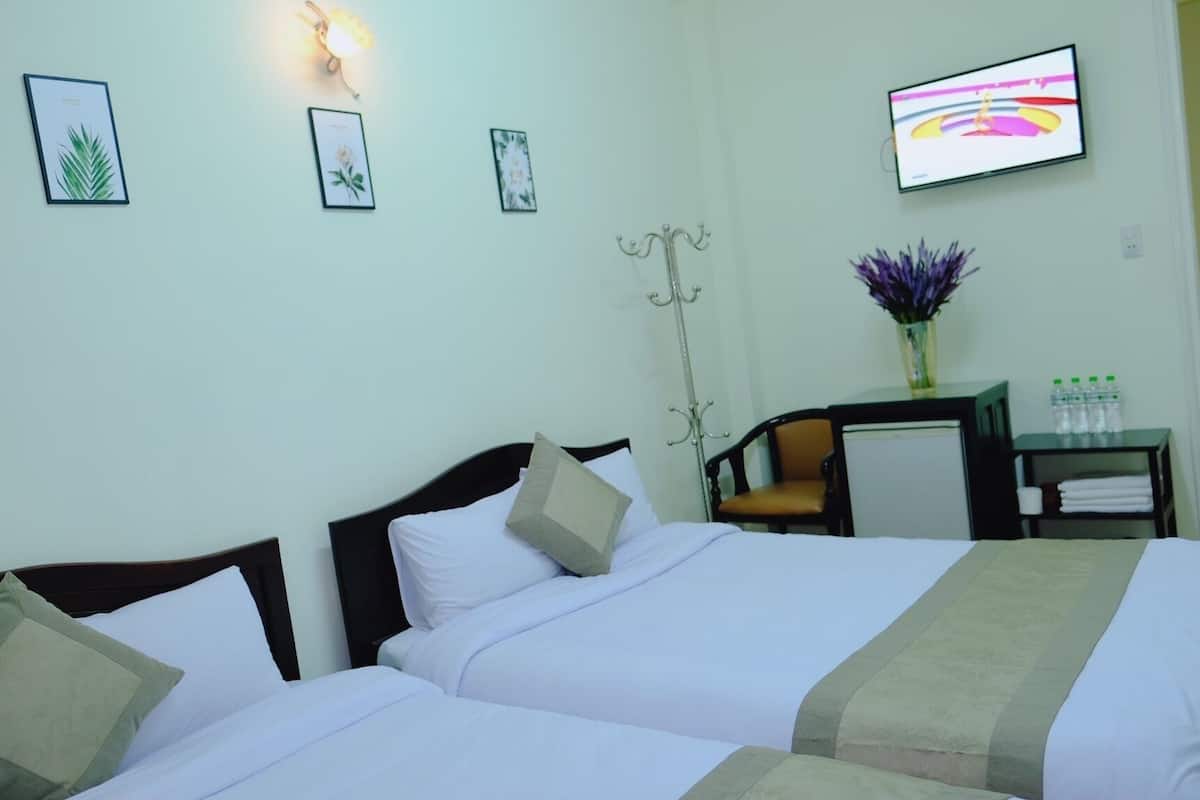 Habitación de hotel con dos camas, un escritorio, una silla, un televisor y un florero con flores.
