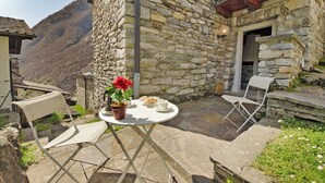 A stone building with a small patio area featuring a table with a chair, a potted plant, and a cup.