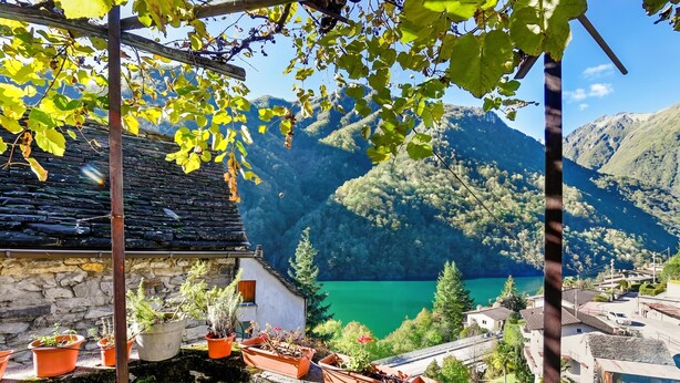 A stone building with terraced potted plants, a clear view of a lake, and surrounding mountains.