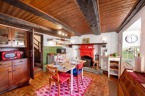 A rustic kitchen with wooden beams, a red fireplace, and a dining area with a red and white patterned rug. - Casa Carla 2 Stone House with Balcony, Vogorno, Switzerland (Vogorno)
