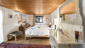 A bedroom with a wooden ceiling, a bed with white linens, a dresser, a bench, and a large mirror.