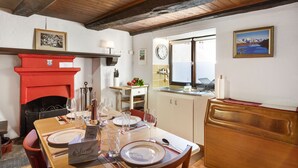 A dining area with a wooden table set for four, a red fireplace, and a view of the sea through a window.