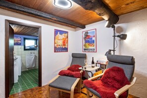A cozy room with two armchairs, a small table with a bottle and glasses, and a poster on the wall.