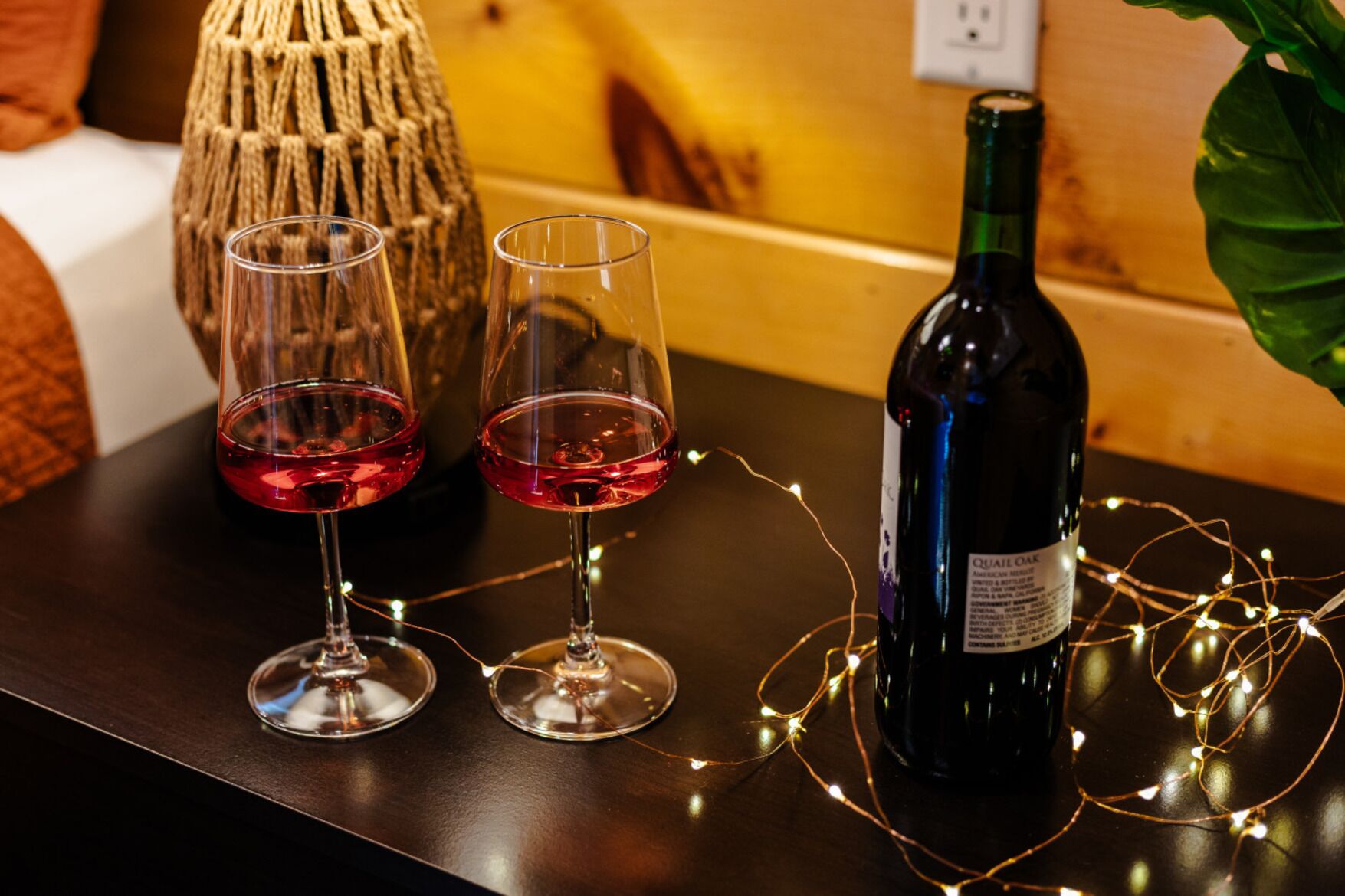 A table with two wine glasses and a bottle of wine, surrounded by string lights.